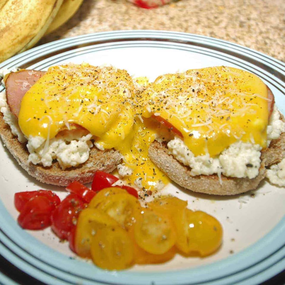 Eggs Benedict with ham, cheese, and scrambled eggs on English muffins, served with cherry tomatoes.
