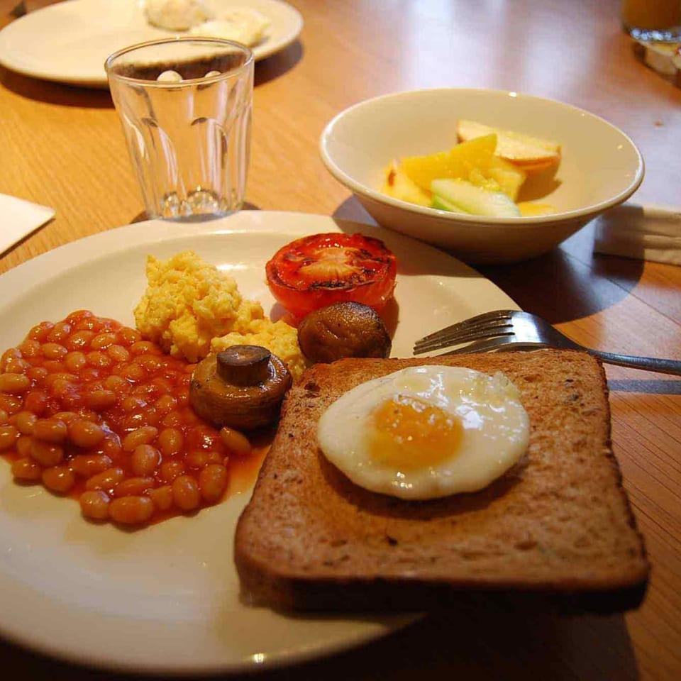 A full English breakfast with baked beans, scrambled eggs, mushrooms, tomato, and fried egg on toast.