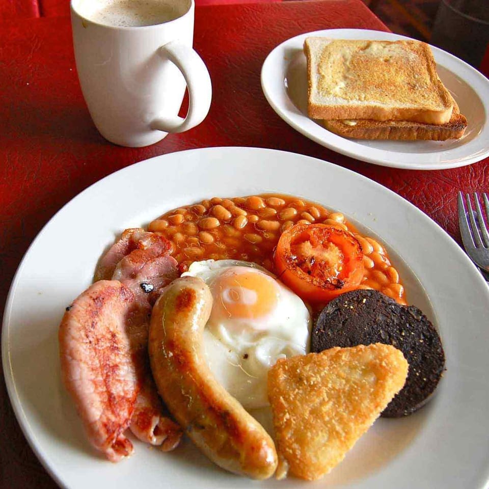 A full English breakfast with sausage, bacon, egg, beans, hash brown, black pudding, and toast.